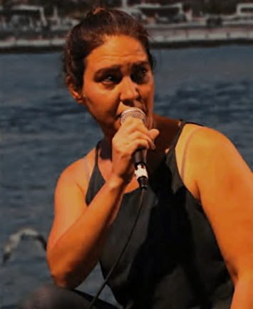 A Turkish woman wearing a black top hold a microphone to her mouth