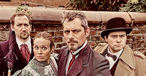 A sepia photograph of four people dressed in Victorian clothes look intensely at the camera