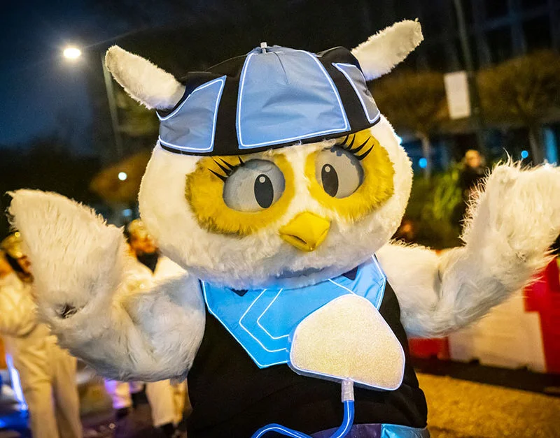 A photograph of someone dressed in an Owl mascot costume wearing blue and black, arms outstretched