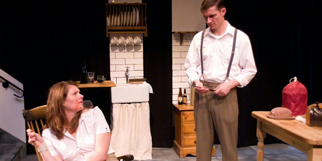 Seen from a play with two people wearing white shirts in a kitchen set
