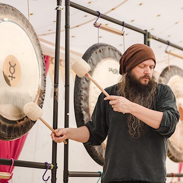 A bearded man wearing a beanie striking a gong