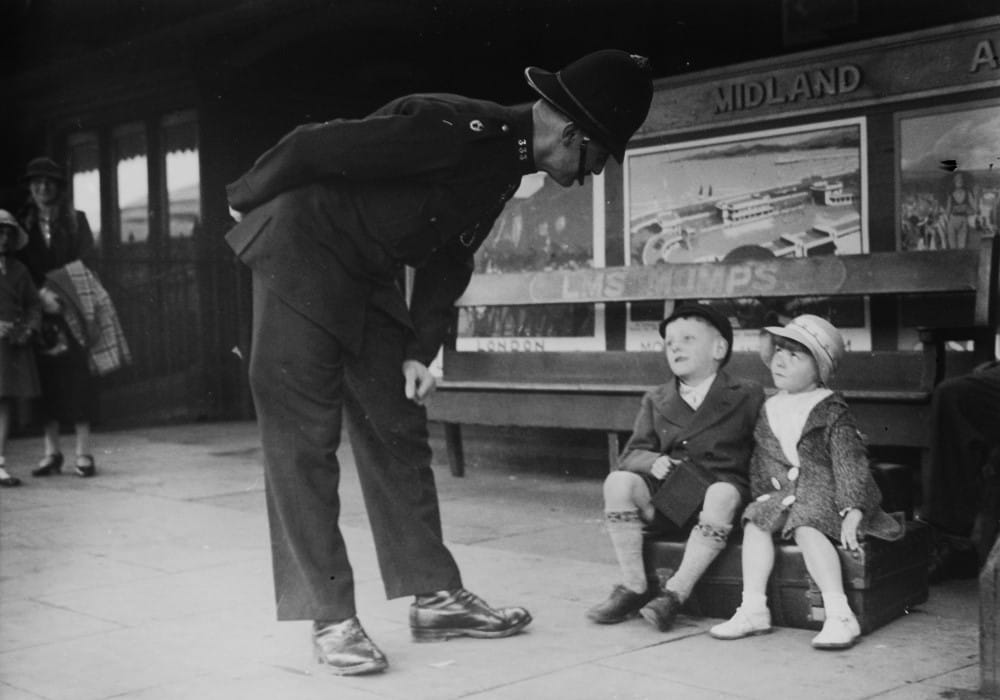 Policeman looking down at two children sat on a bench at Oldham Mumps train station.